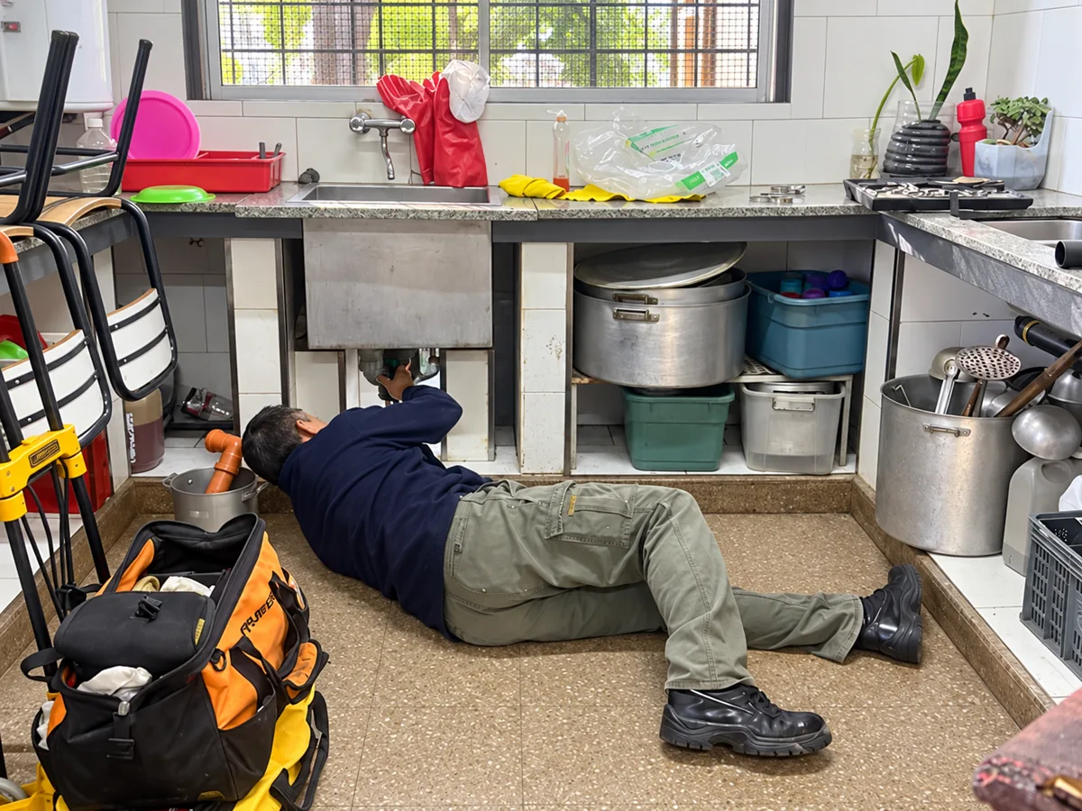 Técnico trabajando en una cañería bajo una pileta de cocina.